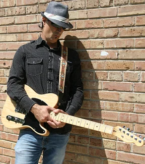 Steve holding guitar looking down by brick wall